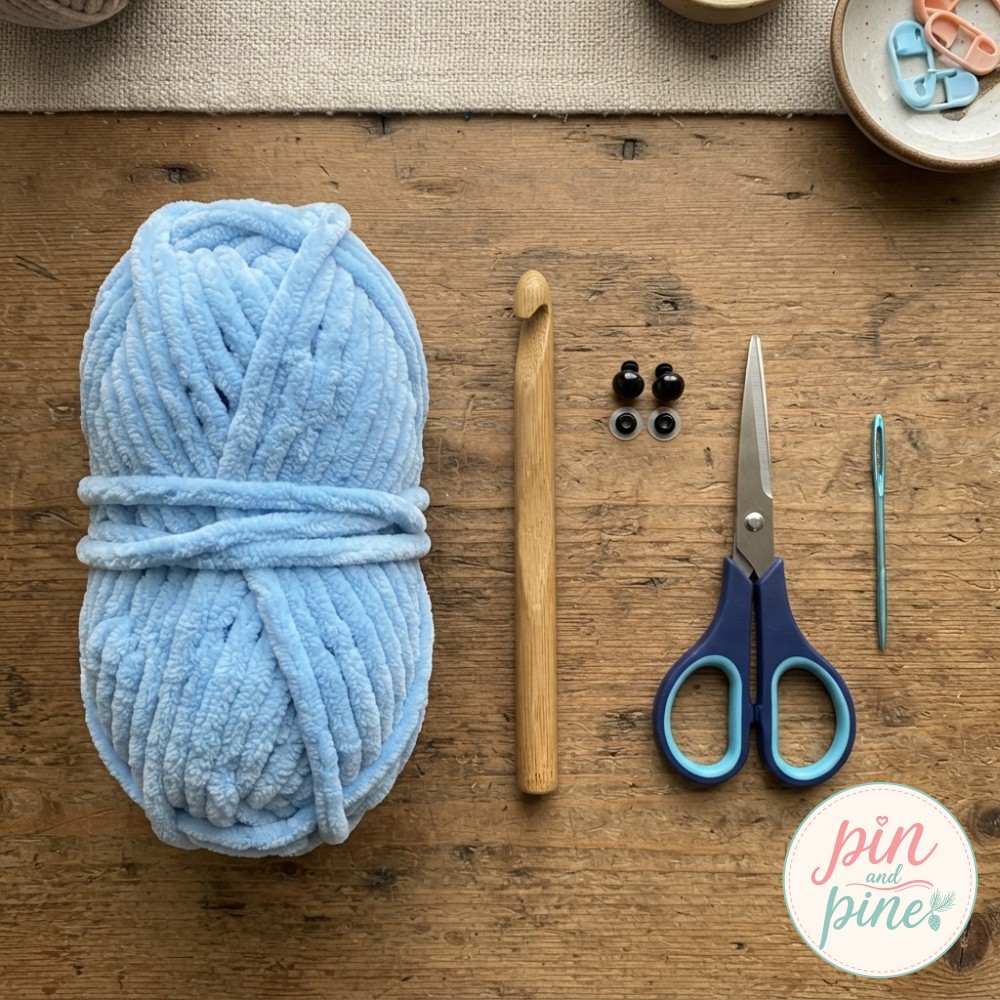 Flat lay of chunky blue yarn, a wooden hook, and safety eyes ready to begin a mini crochet octopus.